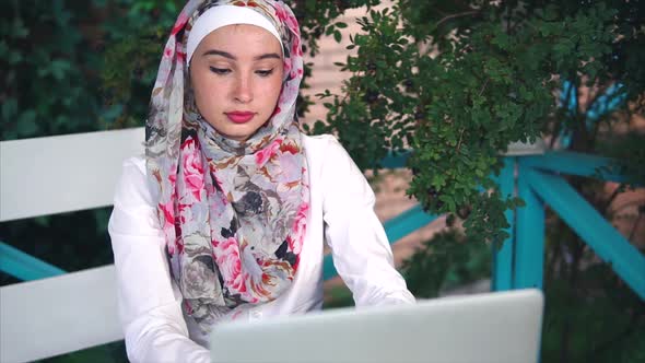 Muslim Woman in Hijab Prints Message on a Laptop, She Is Outside in the Open Air