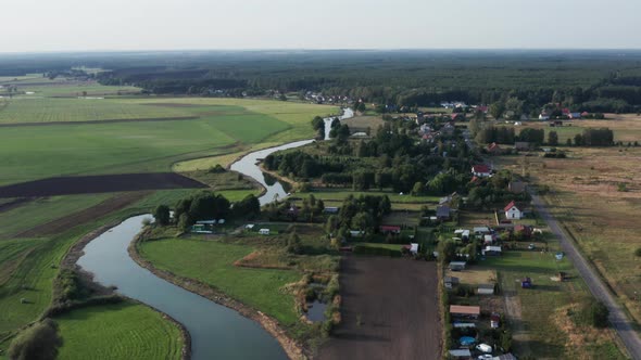 Aerial countryside sunset shot of a small curvy river running by a small farming village, the fields