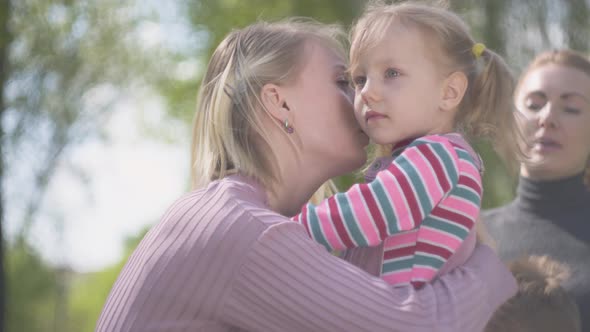 Portrait Blond Young Woman Hugging and Kissing Her Daughter in Sun Light Close Up. Happy Family