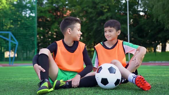 Two Football Players Sitting on the Artificial Green Covering of Outdoors Sport Field