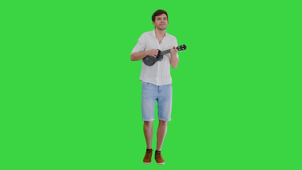 Smiling Young Man Playing Ukulele and Singing Looking Into the Camera on a Green Screen, Chroma Key.