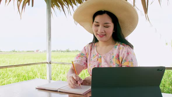 Young woman working with her digital tablet outside her home. In the background rice plantation.