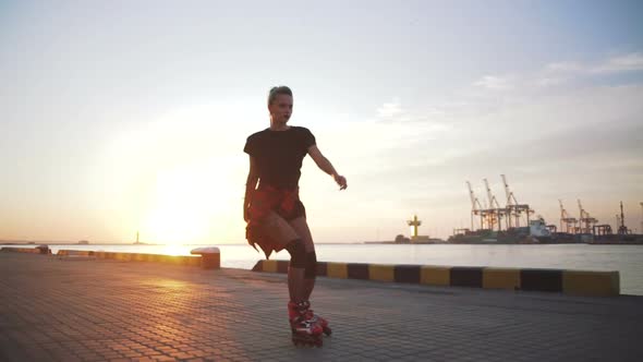 Young Stylish Funky Girl with Green Hair Riding Roller Skates and Dancing Near Sea Port During