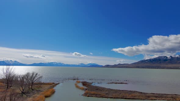 Huge lake with mountains in the background - aerial view pull back shot flying close to the tree bra