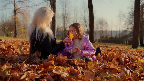 Mother and daughter sitting at autumn forest park. Two females persons spend time together outdoors
