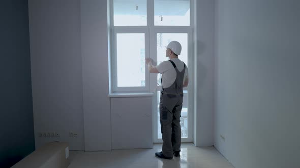 A Builder in Uniform Checks the Size and Quality of Window Installation in a New Apartment