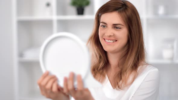 Pleasant Young Beautiful Woman Looking at Mirror Enjoying Natural Beauty at Cosmetology Salon