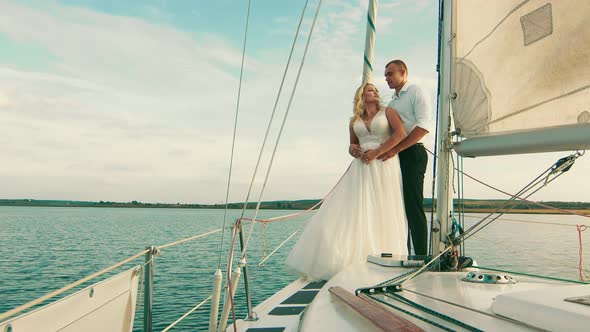 Newlyweds Stand on a Bow of a Sailing Yacht Like in Titani. The Bride Put Her Head on the Groom's