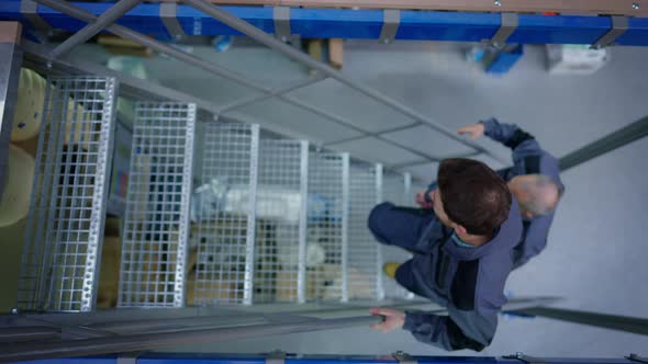 Top View of Young and Senior Caucasian Men Walking Up the Ladder in Industrial Warehouse