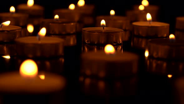 Many small candles burn on a black background