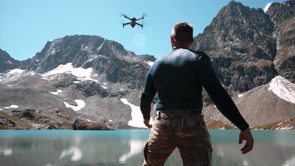 A young man with an athletic physique launches a drone from his hands near a mountain lake