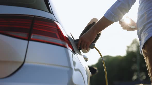 Male Unplugging Electric Car From Charging Station Using Smart Phone App