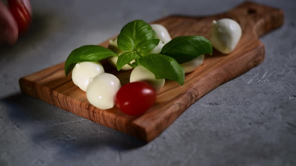 a hand puts the fresh tomatoes on a cutting board with mozzarella cheese