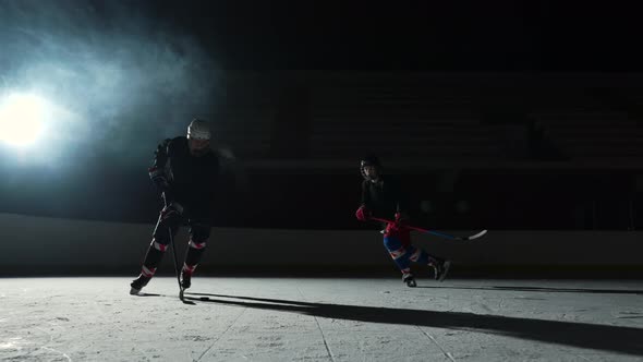 Two Sportsmen Hockey Players Who are Sliding on Ice Arena and Dribbles Hitting Puck with Stick