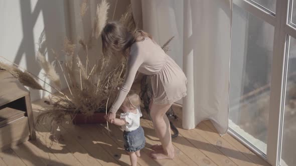 Cute Woman and Her Baby Girl Standing on the Floor at Home. The Child Making First Step, Mother