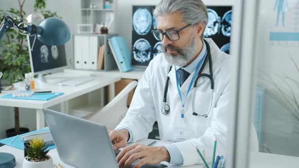 Experienced Doctor Wearing White Gown Using Laptop Typing Concentrated on Routine Work