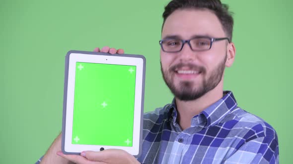 Face of Happy Young Bearded Hipster Man Showing Digital Tablet