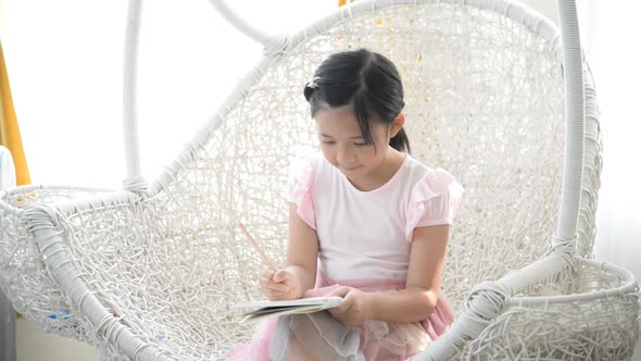 Little Asian Girl Thinking And Writing On Nest Swing