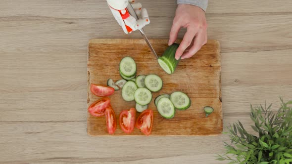 Man With Robotic Prosthetics Hand With Knife On It Is Trying To Cut Cucumber For Slices On Wooden