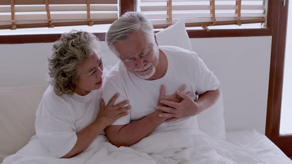 Asian elderly couple in bed, man's heart aches due to heart disease.