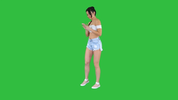 Cute girl checking her cell phone and dancing on a Green