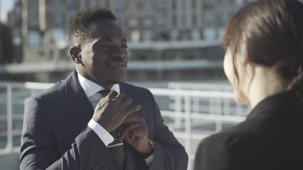 Young Confident Man Adjusting Necktie and Talking To Caucasian Woman Outdoors. Portrait of Handsome