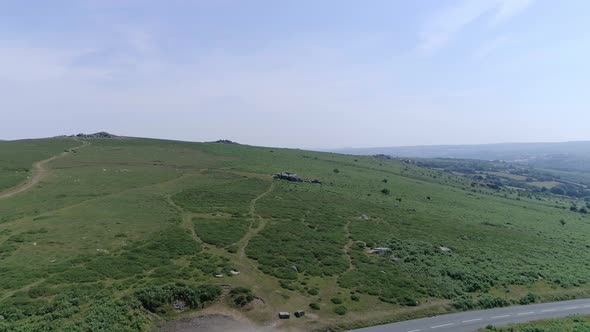 Wide aerial tracking forward over the vast wilderness of Dartmoor, crossing over a road and carpark.