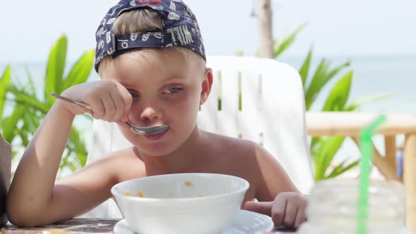 Little Boy Eats Porridge Outdoors. Boy Eating Porridge on the Beach