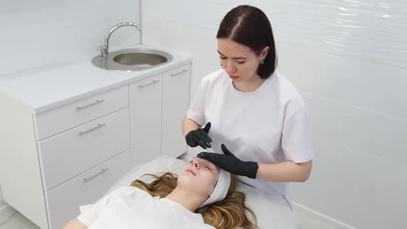 Cosmetologist Applies a Woman a Therapeutic Mask on Her Face