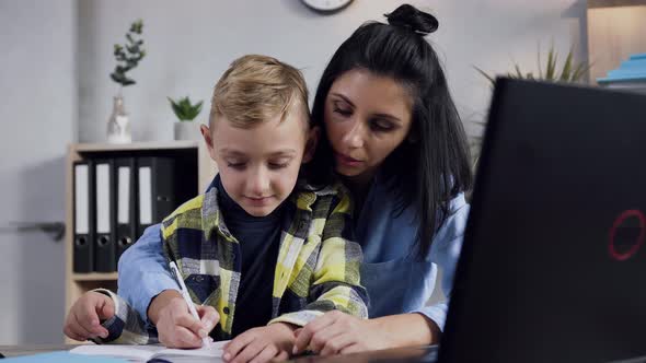 Young Dark Hair Woman Writing Something in the Notebook Together with Her Smiling Teen Boy