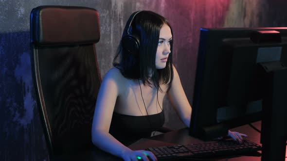 Serious Woman Gamer Playing Online Game on a Pc Computer Wearing Headset and Talking with a Team