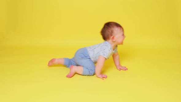 Happy toddler baby boy crawls on studio yellow background. Smiling baby crawling fast on the floor,