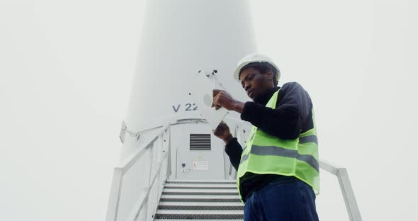 A Man in a Work Uniform is Diagnosing a Wind Turbine Using a Digital Tablet