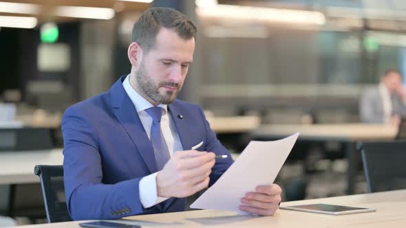 Middle Aged Businessman Reading Documents in Office