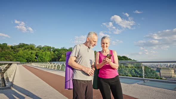 Elderly Man and Woman Watch Photos on Smartphones Walking