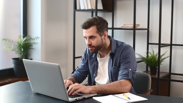 Excited Lucky Young Bearded Freelancer Sitting at the Desk with Laptop