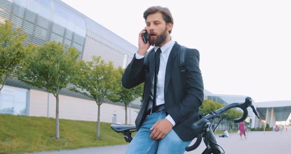 Bearded Man in Stylish Clothes Standing Near His Bike and Talking on Phone