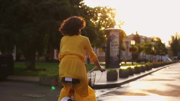 Back View of an Unrecognizable Woman Riding a Citybike with a Basket and Flowers in the City Center