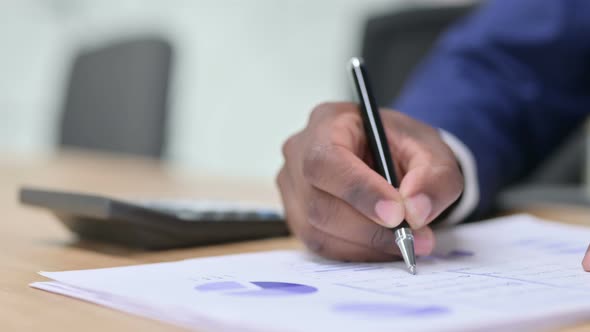 African Businessman Using Calculator for Paperwork, Financial Documents