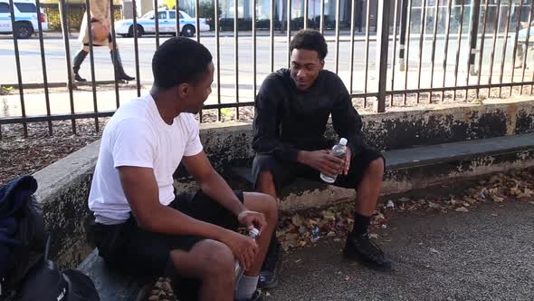 Two young basketball players drinking water while taking a break from playing.