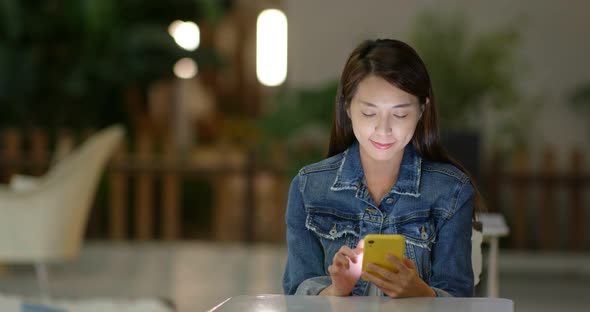 Woman use of mobile phone at outdoor cafe at night