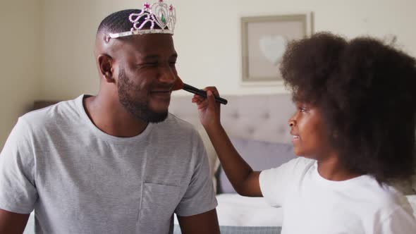 African american father wearing tiara having makeup put on by his daughter