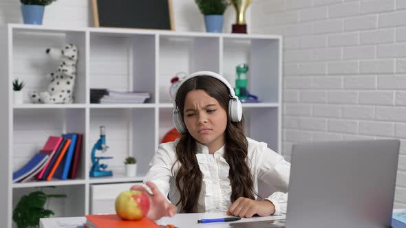 Sleepy Bored Kid Staring to Play with Apple at Lesson Online in Headphones Elearning