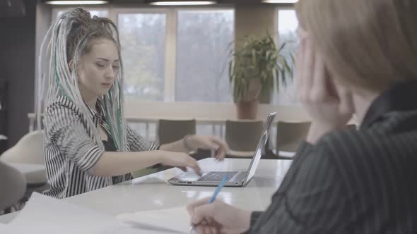 Overworked Young Woman with Dreadlocks Typing Closing Laptop and Looking at Blurred Coworker Writing