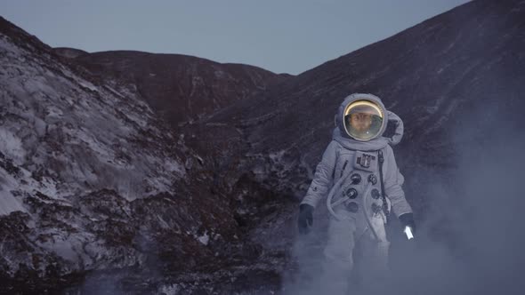 an Astronaut at Dusk with a Lantern Walks Down the Hill Through a Cloud of Steam