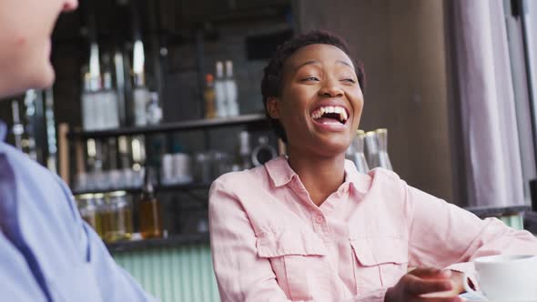 Two happy diverse male and female friends sitting in cafe drinking coffee, talking and smiling