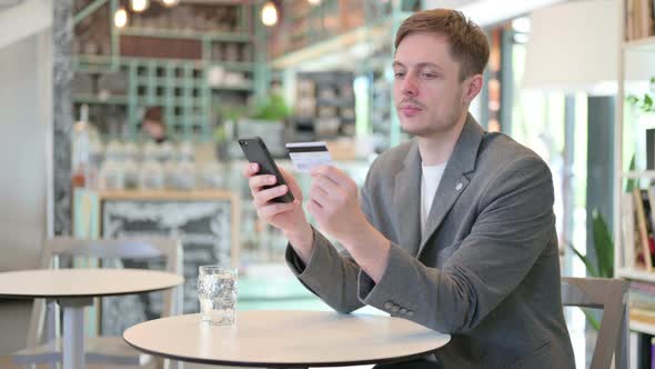 Young Man Making Online Payment on Smartphone in Cafe