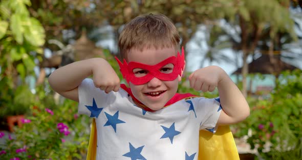 Portrait of a Cute Funny Child Boy in a Superhero Costume in a Red Cloak and Red Mask Plays a