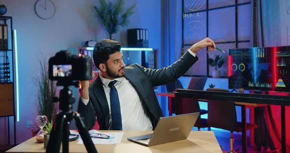 Businessman Explaining Economic Chart on Glass Board Using Camera in Evening Office