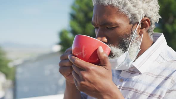 Senior man with face mask on his chin drinking coffee